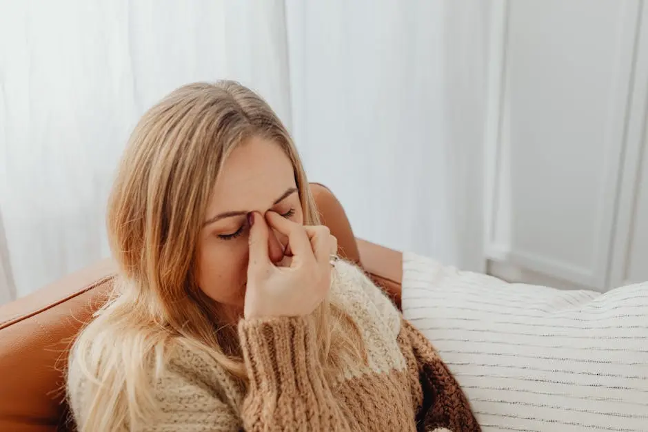 A woman sitting on a couch with eyes closed, holding her nose in apparent sinus pain.